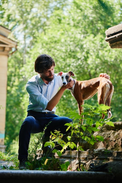 Man in shirt and trousers sitting in a Park and looking at the dog