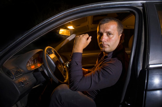 A man in a shirt with a phone in a car at night