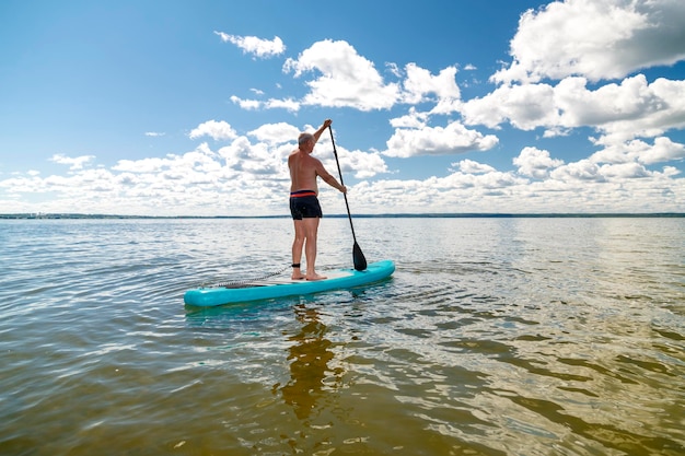 A man in shorts on a SUP board with an oar floats standing on the water against the blue sky