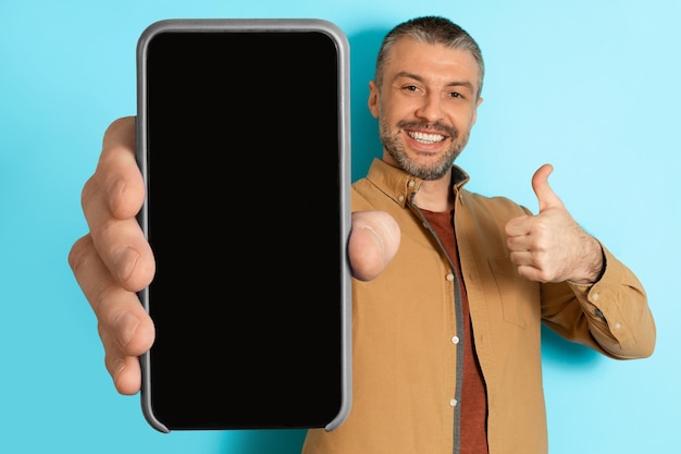 Man showing huge cellphone gesturing thumbs up over blue background