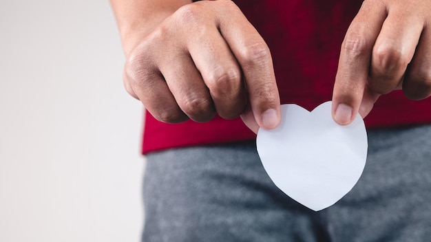 The man shows a paper heart at downside of body Close up shot with copy space