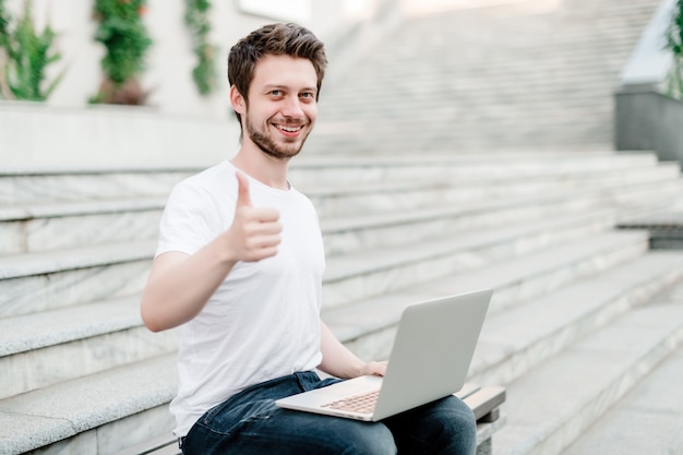 Man shows thumbs up with laptop on the stairs