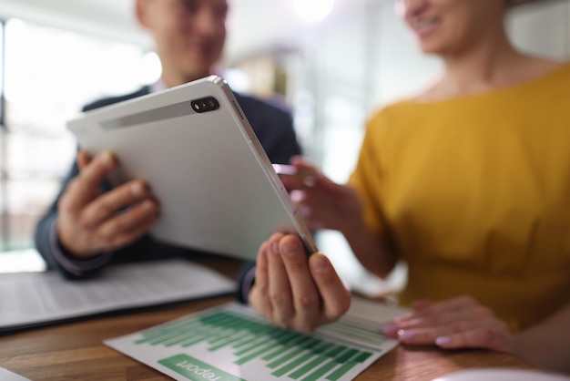 Man shows woman accounting information on website via tablet happy colleagues sit at table in