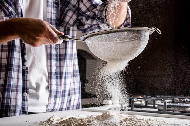 A man sifts flour through a sieve to make fresh bread Wheat flour of the highest grade for bread Flour aeration