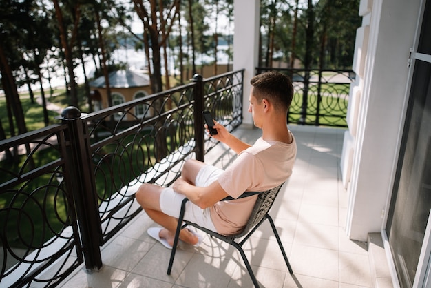 A man sits on a chair and holds a cell phone on the balcony