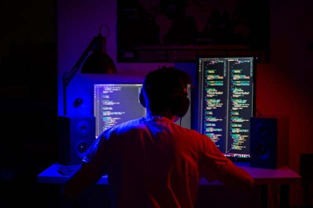 A man sits at a computer in a room at a table at night with blue lighting and programs