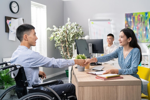 Man sits at desk in an office use wheelchair opposite him beautiful woman in dress asks questions