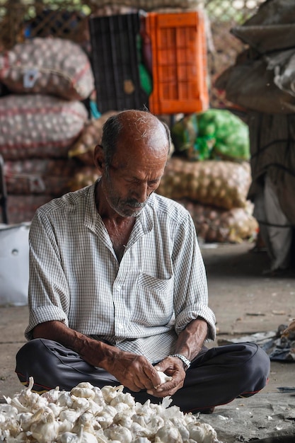 A man sits on the floor in front of a pile of bags of produce.