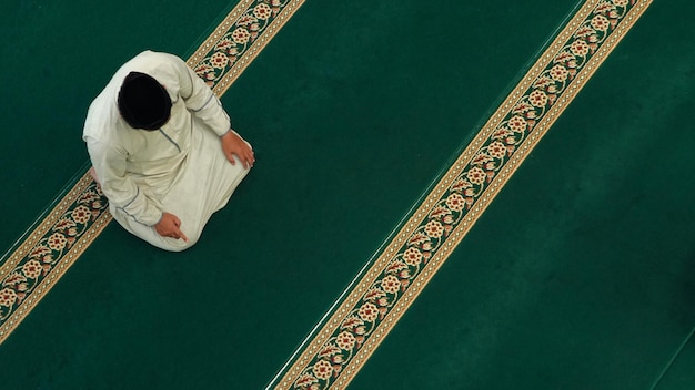 A man sits on a green carpet in a mosque.