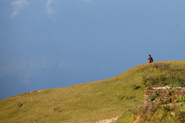 A man sits on a hill in front of a blue sky.