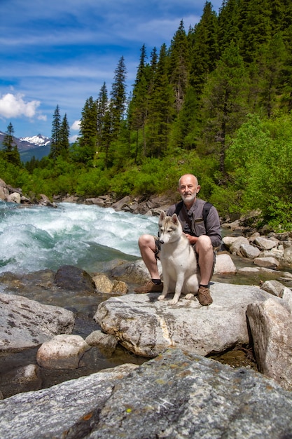 A man sits near the river with his dog