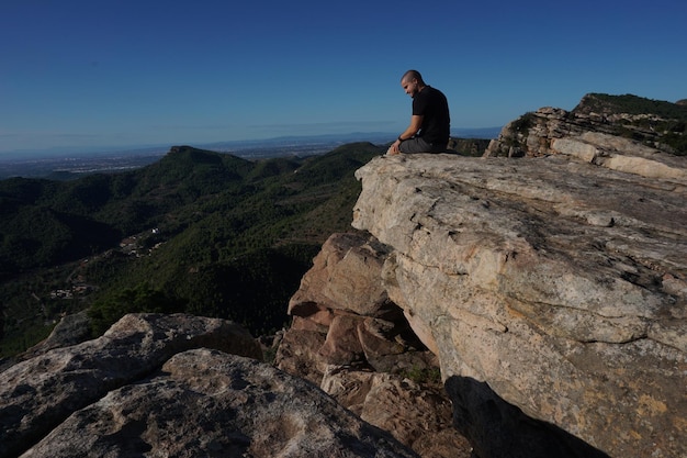 A man sits on a rock overlooking the mountains.