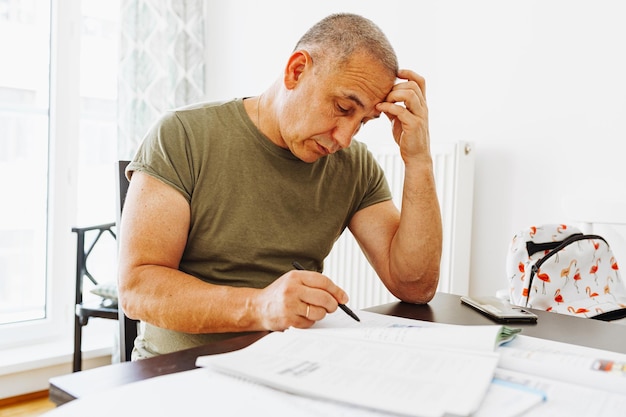 A man sits at a table, writing a letter with a pen.