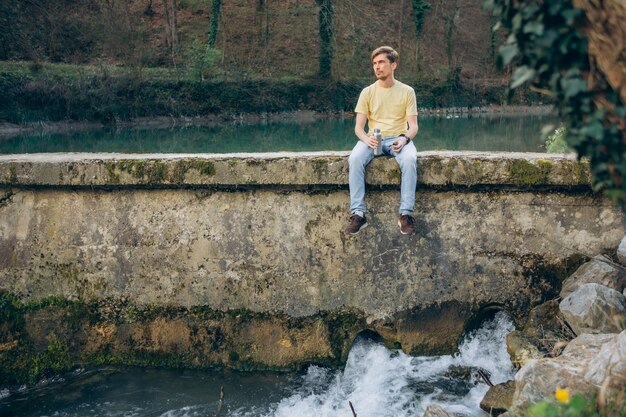 Photo a man sits on a wall in front of a river.