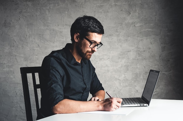 A man sits with a laptop in a black shirt. Business concept, work. Office routine. Property efforts