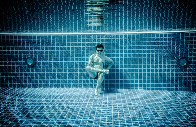 Man sitting on the bottom of the swimming pool under water