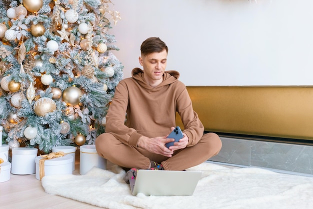 A man sitting on floor near Christmas tree orders online goods on black friday