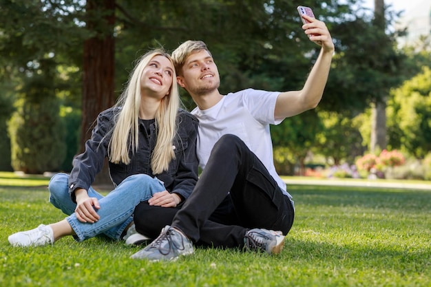 A man sitting on the grass with his girlfriend and taking selfie