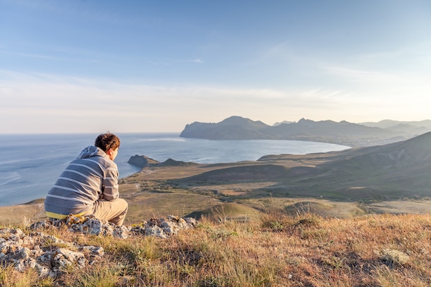 Photo man sitting on a hill above the city meditating and watching the sunset