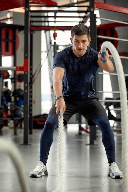 Man sitting on his toes holding a pair of battle ropes for workout guy at the gym working out with fitness rope