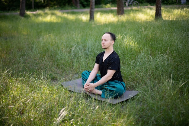 Man sitting lotus position practicing yoga in the park on green grass