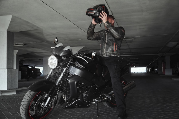 A man sitting on a motorcycle takes off his helmet in underground parking garage in motion