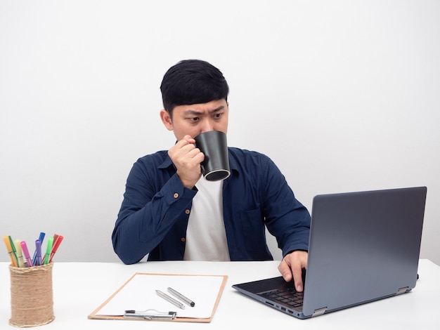 Man sitting at office workplace drinking coffee with using laptop for working