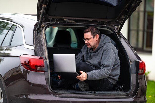 Photo a man sitting in the open trunk of a car and working on a laptop technology to work remotely