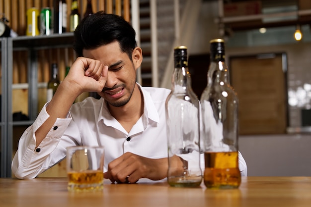 A man sitting at the pub is crying due to his sadness and want to forget it by drinking alcohol.