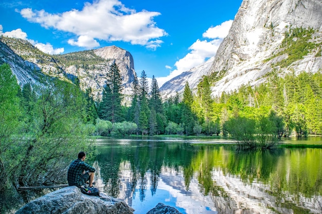 Photo man sitting on rock by lake against mountains and sky