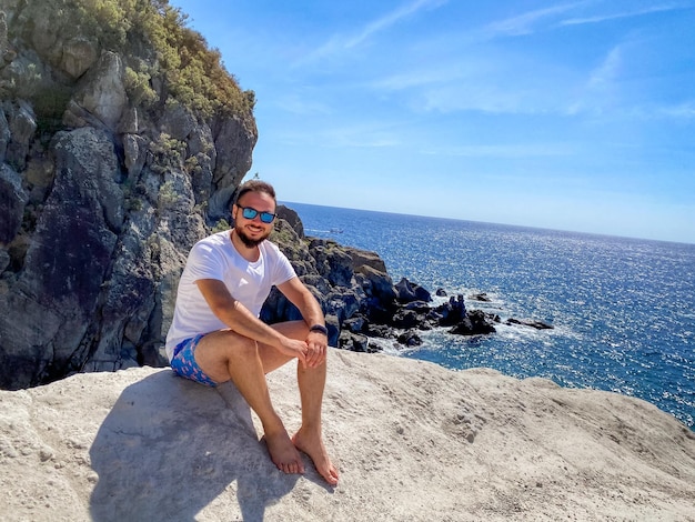 Photo man sitting on rock by sea against sky