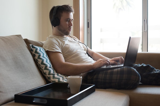 Man sitting on sofa with headphones and laptop