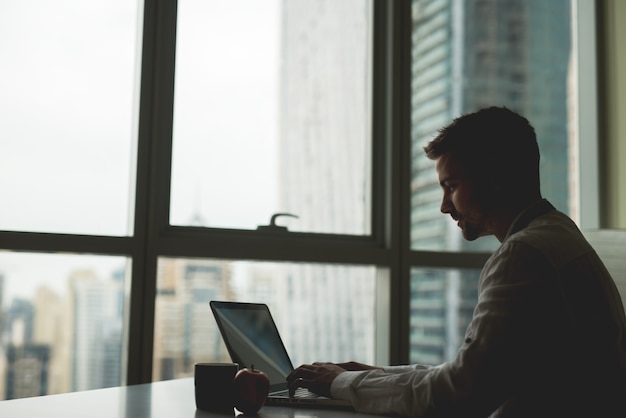 Man sitting at table next to panoramic window with magnificent city view.