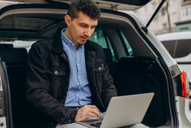 Photo man sitting in trunk of his car and working on computer