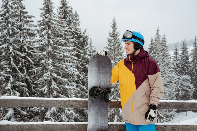 Man in ski equipment, wearing safety glasses, stands against mountain and trees. Winter sport and recreation, leisure outdoor activities.