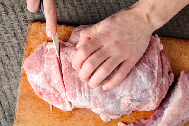 Man slices meat into pieces with a knife on cutting board on a dark surface