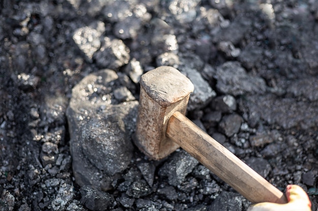 A man smashes large pieces of coal with a sledgehammer mineral solid fuel for stoves and fireplaces