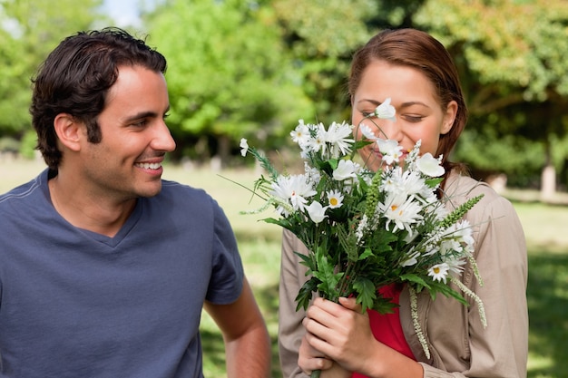 Man smiling as he watches his friend smell a bunch of flowers