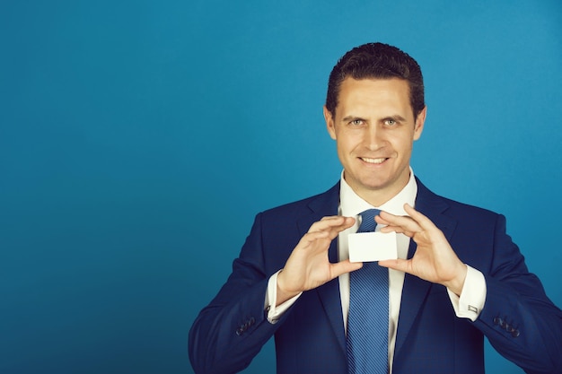 Man smiling and holding card in business suit on blue