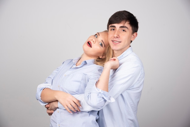 Man smiling and hugging his girlfriend against gray wall .