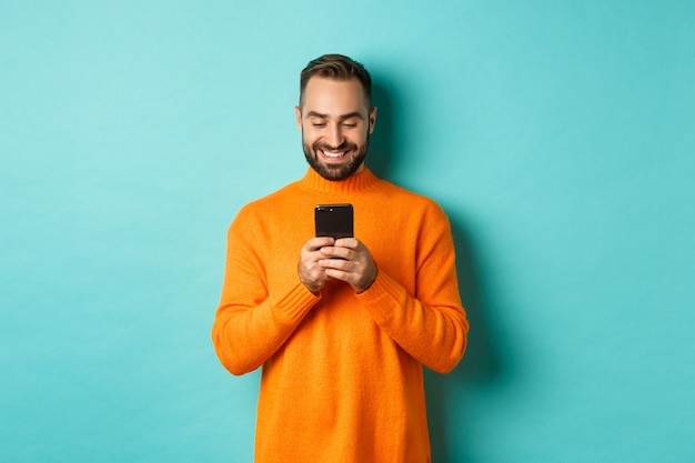  man smiling and texting message on mobile phone, communicating online, standing over light