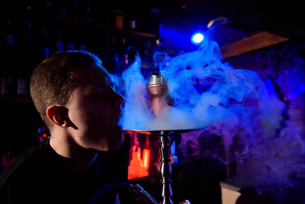 Man smoking traditional hookah pipe and exhaling smoke in hookah cafe.