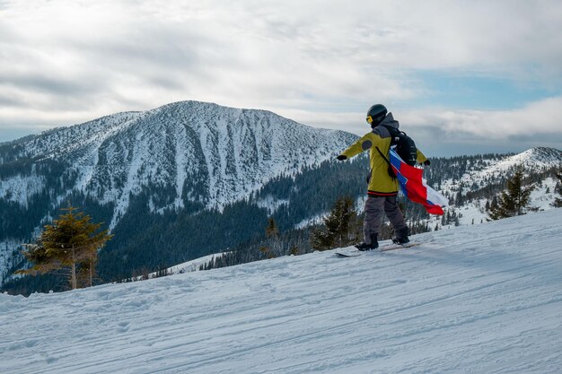 Man snowboarder with slovakia flag at ski resort slope beautiful mountains landscape on background