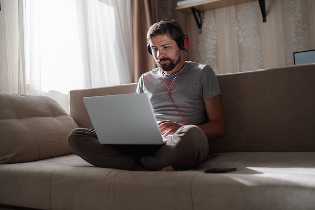 Man on sofa with headphones and notebook at home