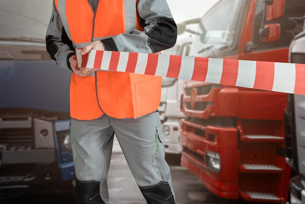 Man in special clothes blocks the parking with a tape different semi trucks on the background