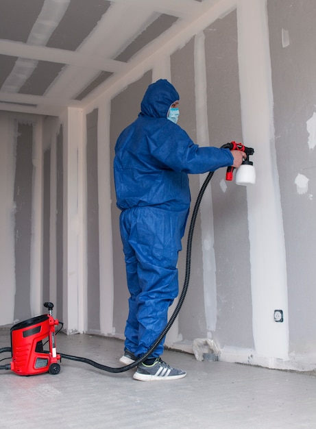 A man in a special suit paints walls with a spray gun, painting walls and ceilings