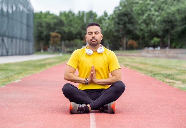 man in sportive wear meditating sitting in lotus pose on running track at outdoor urban stadium