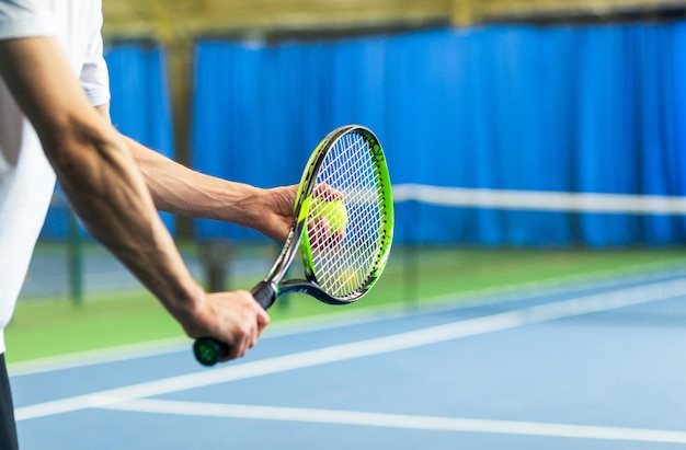 A man in a sports uniform holds a racket and a ball in his hands and is about to serve Hands close up Horizontal photo