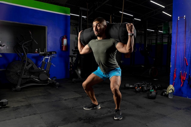 Man in sportswear in a gym doing squats with a sandbag on his back