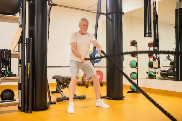 Man in sportswear pulling the ropes in gym